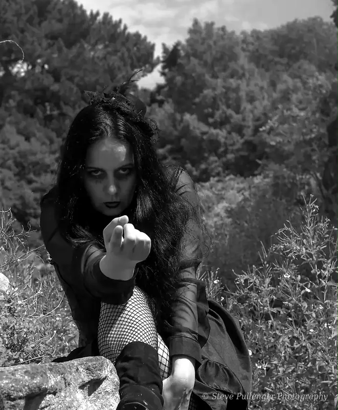 Black and white portrait of a woman in gothic dress reaching towards the camera outdoors