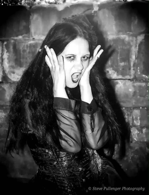 Black and white portrait of a woman screaming with her hands on her face against a brick wall