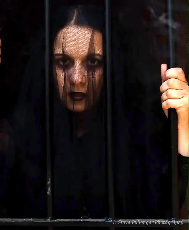 Woman with dark veil make-up gripping iron bars and staring into the lens