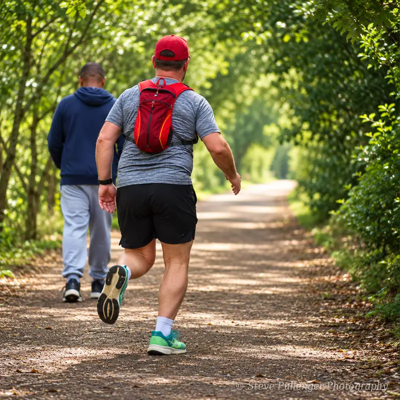 Runner in a red cap and backpack jogging along a leafy woodland path