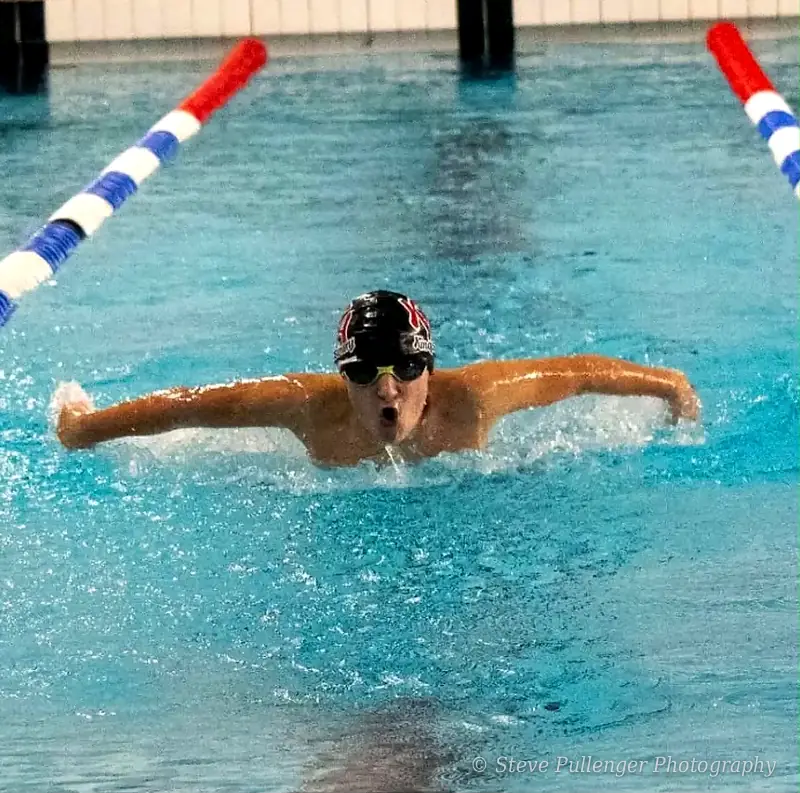 Swimmer powering towards the camera in butterfly stroke between lane ropes